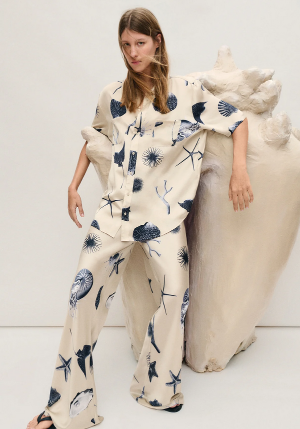 Woman wearing a cream outfit with blue patterns sitting on a white couch.