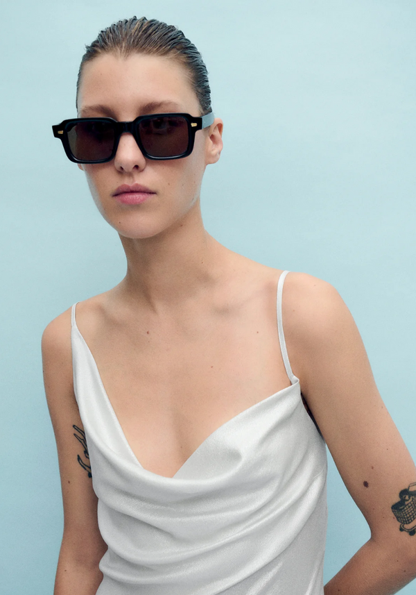 Woman wearing a white top and black sunglasses against a light blue background