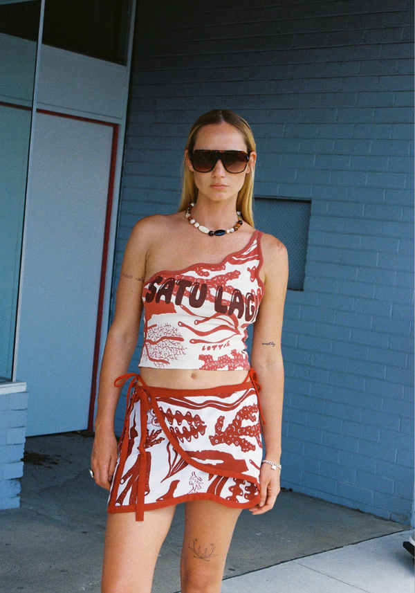 Woman wearing a red and white outfit with 'Sato Lag' text in front of a blue brick wall.