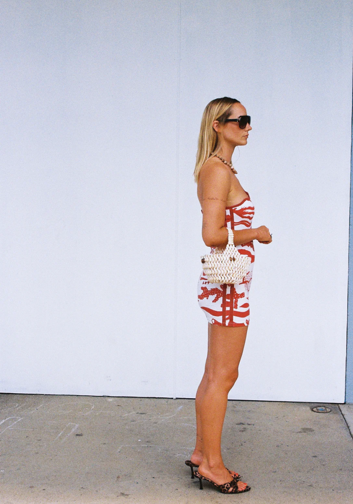 Woman in a red and white patterned outfit with a white bag against a white wall.