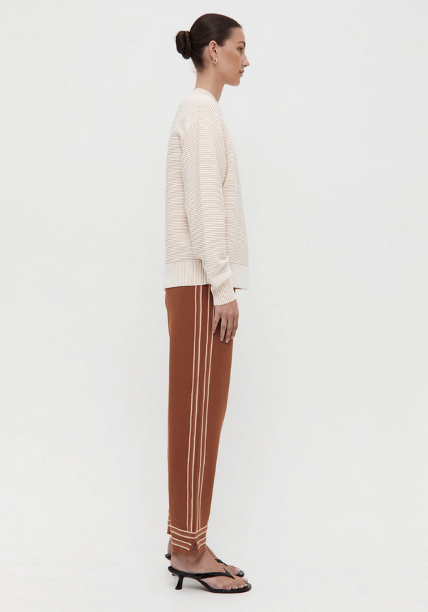 Woman wearing a white blouse and brown pants with white stripes on a white background