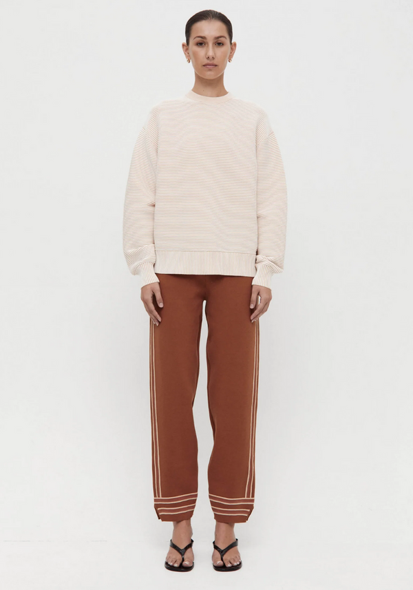 Woman wearing a beige sweater and brown pants with white stripes on a white background