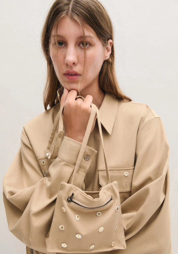 Woman holding a beige handbag against a plain background- Sandro Style Clothing - Khaki Outfit. Tonal Outfits
