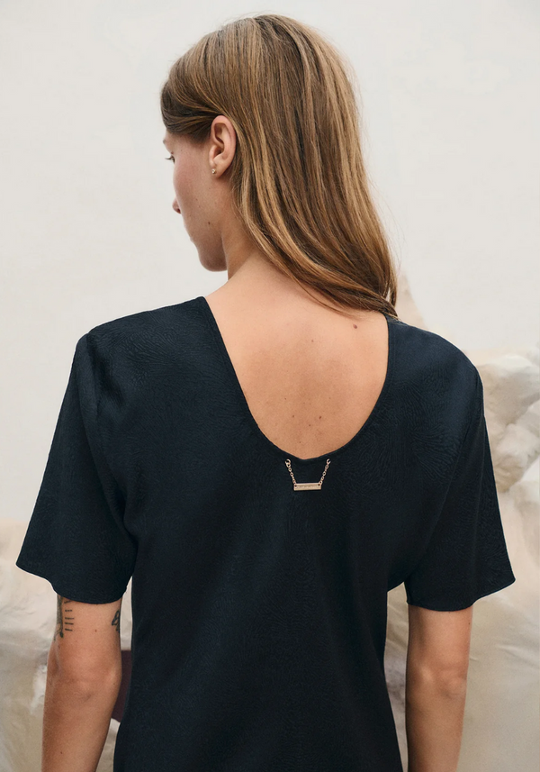 Person wearing a black top with a unique back design on a neutral background