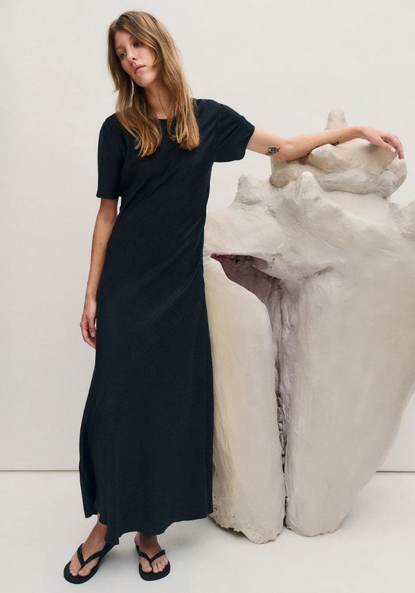 Woman wearing a black dress standing next to a white sculpture on a white background