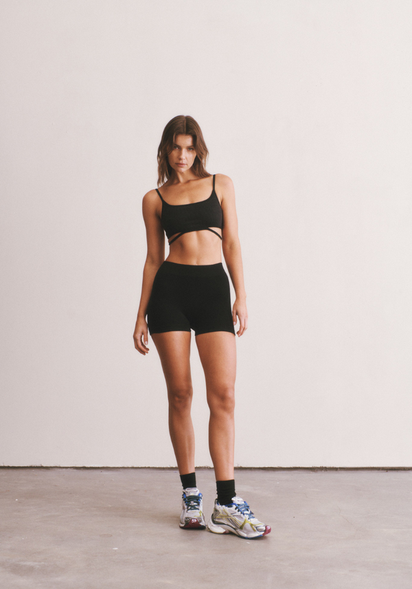 Woman wearing a black sports bra and shorts standing against a plain background