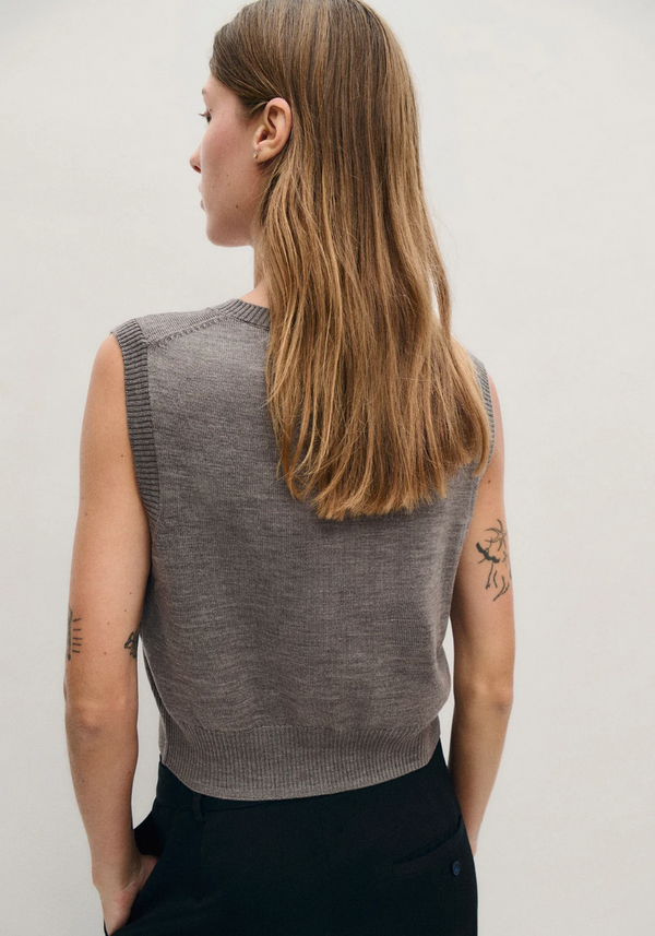 Woman wearing a gray sleeveless sweater against a plain background 