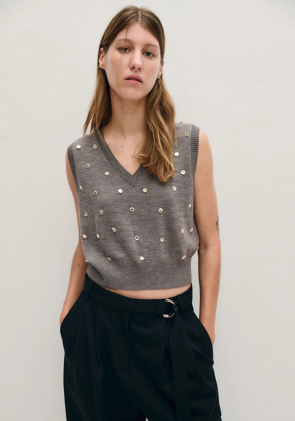 Woman wearing a gray sleeveless top with pearl embellishments against a plain background.