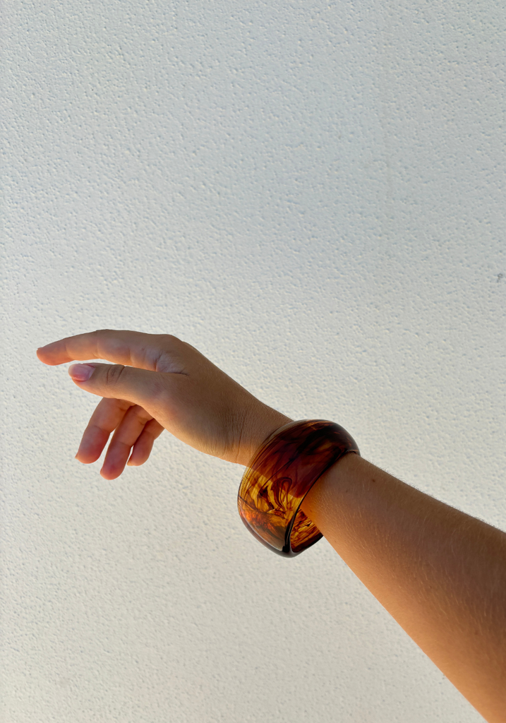Hand wearing a brown bracelet pointing towards a light gray background